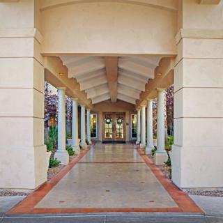 A symmetrical view of a covered walkway with columns and arches leading to a building entrance.