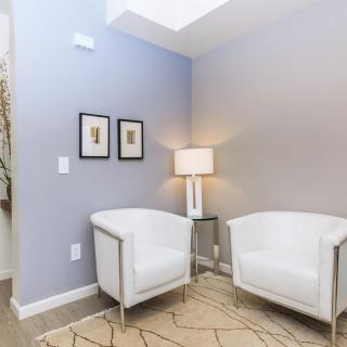 A modern living room corner with white chairs and a lamp.