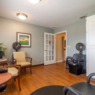 A cozy waiting room with chairs, a painting, and fans on a hardwood floor.