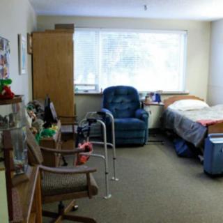 A cozy bedroom with a bed, chair, and walker by the window.