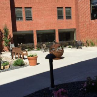 A sunny courtyard with benches, potted plants, and a brick building.