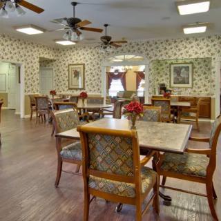 A well-decorated dining room with multiple tables and chairs, featuring wallpapered walls, wooden floors, and ceiling fans.