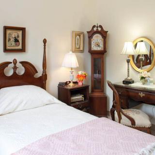 A cozy, traditionally furnished bedroom with a bed, grandfather clock, and desk with a mirror.