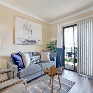 A cozy living room with a stylish sofa, cushions, and artwork, leading to a balcony through a sliding glass door.