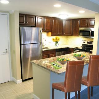 A modern kitchen with stainless steel appliances and granite countertops, featuring wooden cabinets and bar stools.