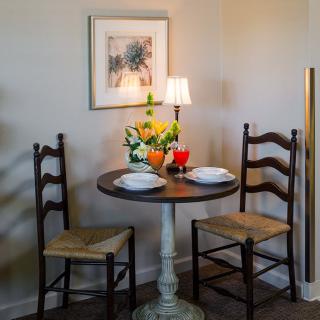 A cozy dining setup with a small round table and two chairs adorned with flowers and a lamp.