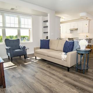 A modern, well-lit living room with a beige couch, armchair, and wooden flooring.