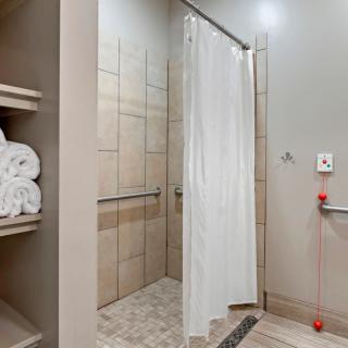 Modern bathroom with a tiled shower and neatly stacked towels on open shelving.