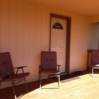 A sunny porch with three chairs and a door.