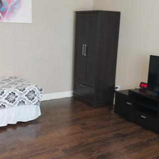 A minimalist bedroom with a small wardrobe, television, and wooden flooring.