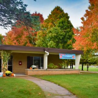 A small building surrounded by colorful autumn trees with a pathway leading to its entrance.