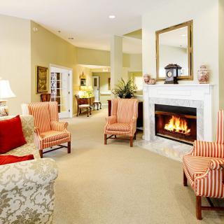 A cozy living room with a lit fireplace, armchairs, and elegant decor.