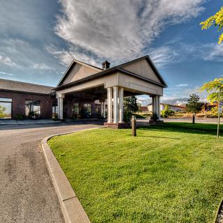 A scenic view of a building with a columned entrance and well-maintained grassy landscape under a partly cloudy sky.