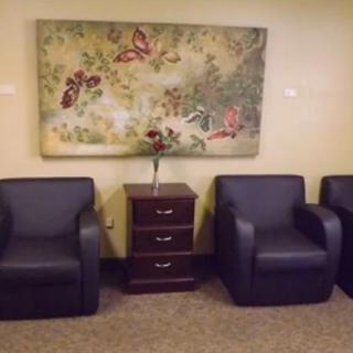 A waiting room with three armchairs, a small table in between, and a floral and butterfly painting on the wall.