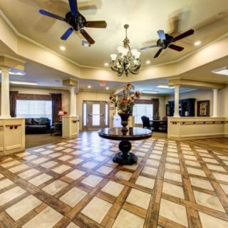 A spacious lobby featuring a central chandelier, ceiling fans, and a decorative table on a patterned wooden floor.