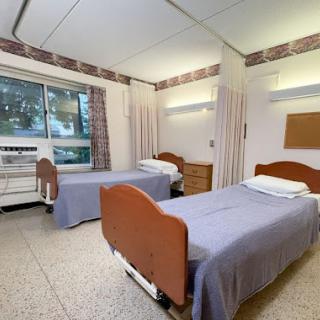 A clean hospital patient room featuring two beds and natural light from a window.