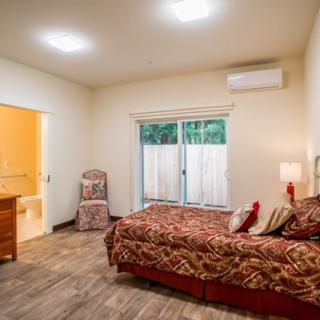A cozy bedroom with patterned bedding and modern lighting, featuring a window and an attached bathroom.