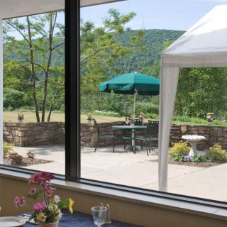 A scenic view from inside, looking out at a patio with tables and umbrellas set against a backdrop of mountains and greenery.