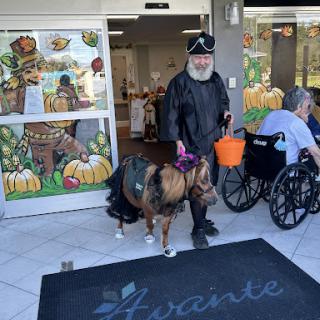 A man in a costume with a dog, celebrating the fall season outside a facility.