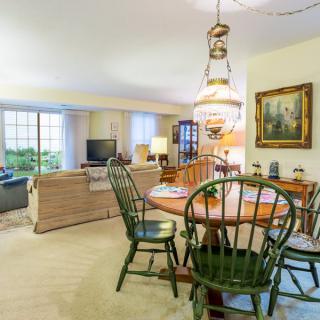 A cozy living and dining area featuring a round wooden table with chairs, a sofa, and decorative elements such as a lamp and painting.