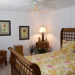 A cozy bedroom with a wooden sleigh bed, floral bedding, and warm lighting from a bedside lamp. The room is decorated with framed artwork and a touch of greenery.
