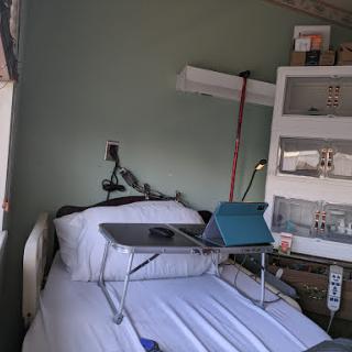 A hospital room featuring a bed with a laptop table set up beside it.