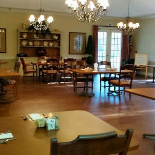 A well-lit dining room with elegant chandeliers and neatly arranged tables and chairs.