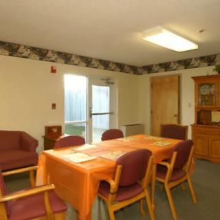 A well-lit dining room with a table covered by an orange tablecloth and surrounded by chairs.