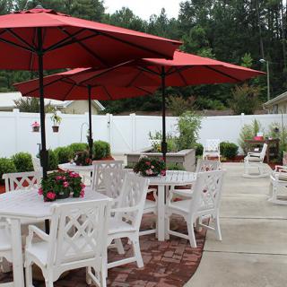An outdoor patio area with tables, chairs, and red umbrellas surrounded by greenery.