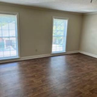 An empty room with hardwood flooring and two large windows allowing natural light to enter.