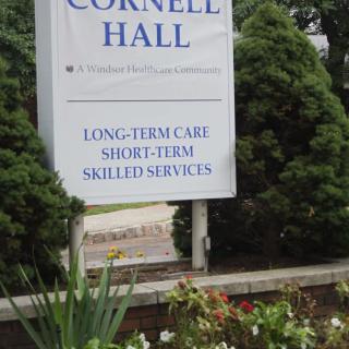 A sign for Cornell Hall, a healthcare facility offering long-term and short-term skilled services, surrounded by greenery.