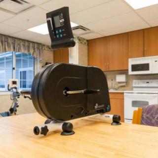 A pedal exerciser placed on a table in a kitchen-like setting, commonly used for rehabilitation and fitness.