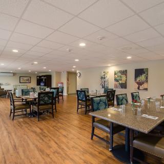 A spacious dining area with neatly arranged tables and chairs, featuring wooden flooring and ceiling lights.