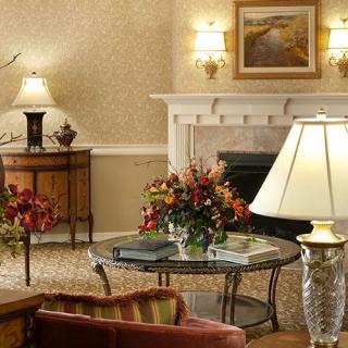 A cozy living room with elegant decoration, featuring a fireplace, lamps, and floral arrangements.