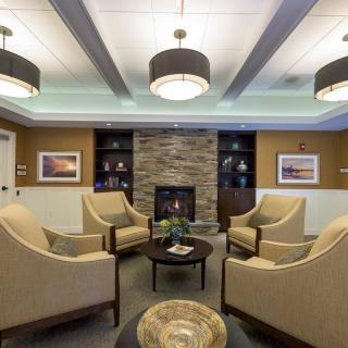 A cozy living room with armchairs arranged around a central fireplace, featuring modern decor and warm lighting.