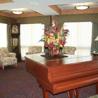 A cozy living room interior featuring a piano, flower arrangement, and a grandfather clock.