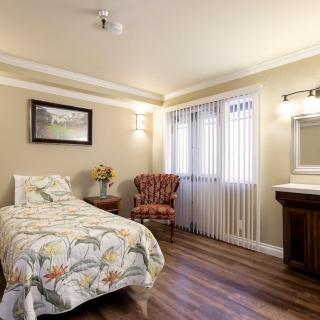 A cozy bedroom with a single bed, an armchair, and hardwood flooring.