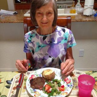A woman sitting at a dining table enjoying a meal consisting of steak, salad, and a baked potato.