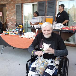 An elderly man enjoys a moment at an outdoor social gathering, surrounded by food and joyful company.