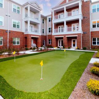 A modern apartment complex with a neatly maintained outdoor putting green surrounded by landscaping.