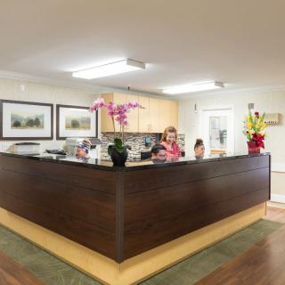 A welcoming office reception area with a wooden desk, decorative flowers, and framed art on the walls.