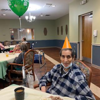 An elderly man enjoying a birthday celebration with a festive party hat and a cheerful atmosphere.