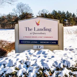 A sign for The Landing at Queensbury, an assisted living and memory care facility, covered in snow.