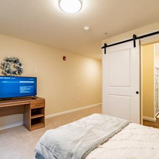 A cozy bedroom featuring a bed, television on a desk, and a sliding barn door leading to another room.