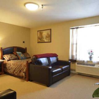 A cozy bedroom with a bed and sofa, featuring warm lighting and simple decor.