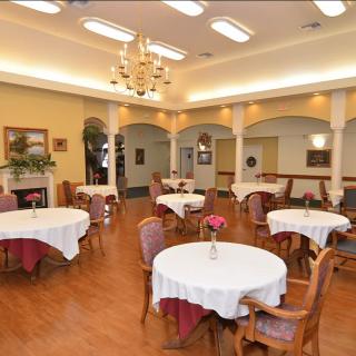 An elegant dining area with round tables and upholstered chairs, featuring a chandelier and classic decor.