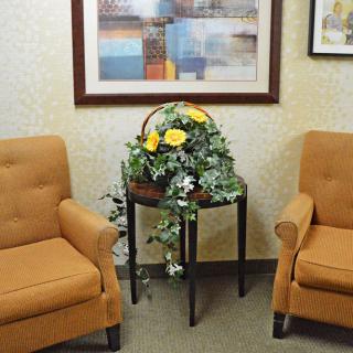 A cozy waiting room with two orange chairs, a side table with a floral arrangement, and artwork on the wall.