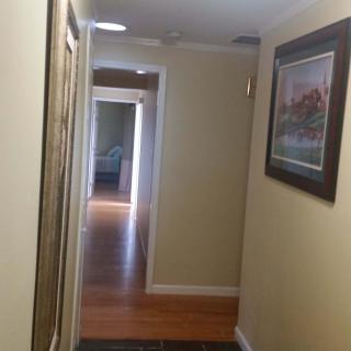 A well-lit hallway with wooden floors, adorned with artwork and leading to an open doorway.