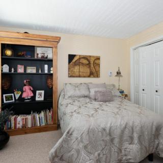 A cozy bedroom with a bed, bookshelves filled with decor and books, and artwork on the walls.