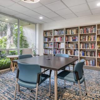 A cozy study room with bookshelves, a table, and chairs by a large window.